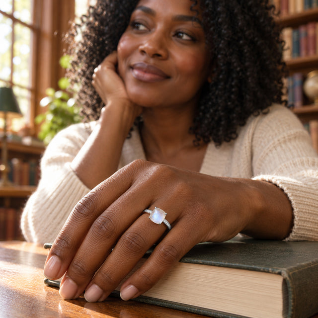 A woman wears the white gold moonstone ring on her hand resting on a closed book in a sunlit library.
