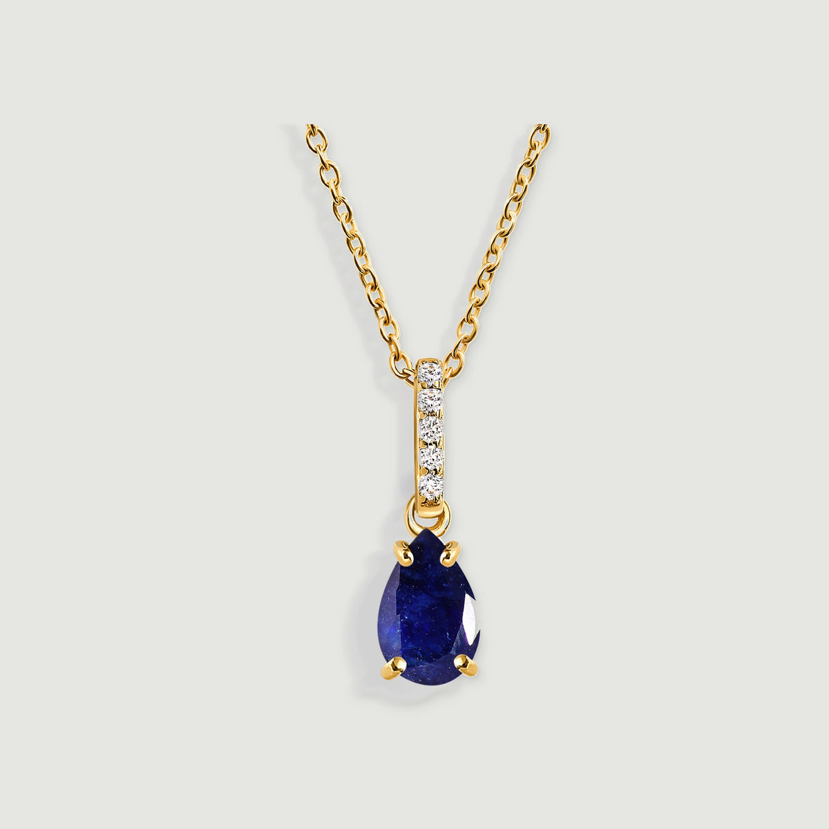 A yellow gold necklace with a pear-shaped blue sapphire and five clear stones rests against a light gray background.