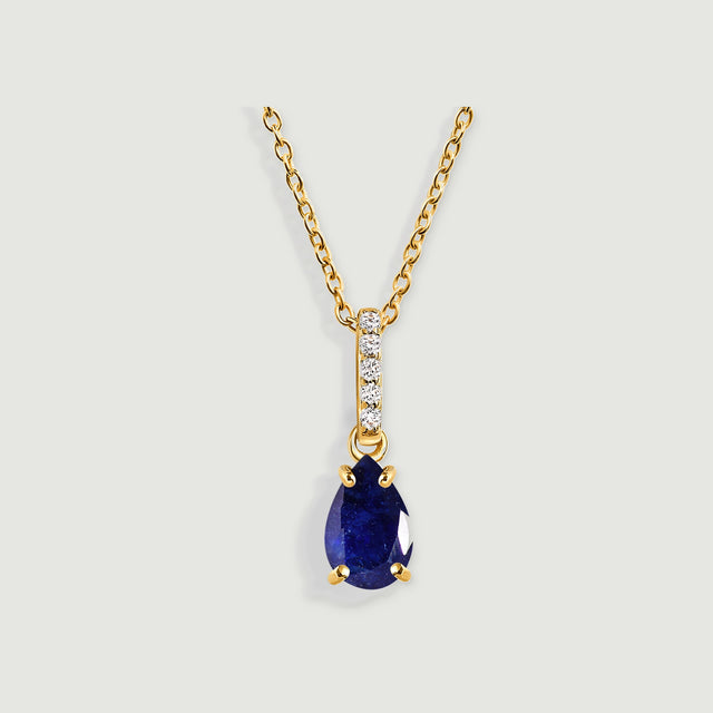 A yellow gold necklace with a pear-shaped blue sapphire and five clear stones rests against a light gray background.