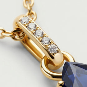 A diagonal gold bail displays five round clear stones beside polished chain links on a light gray surface.
