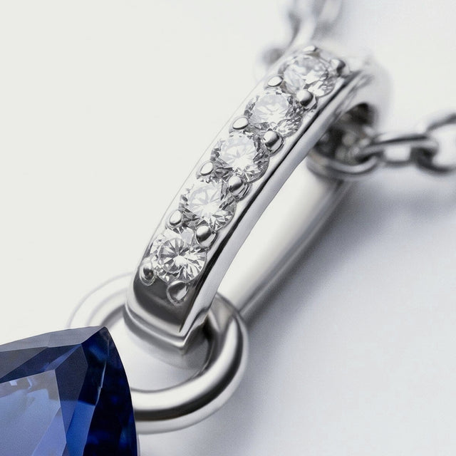 Five bright clear stones run along a silver bail connected to oval chain links above the tip of a blue sapphire.