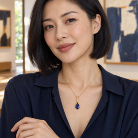 A woman with a black bob wears the yellow gold sapphire necklace above a navy blouse in a gallery with abstract paintings.