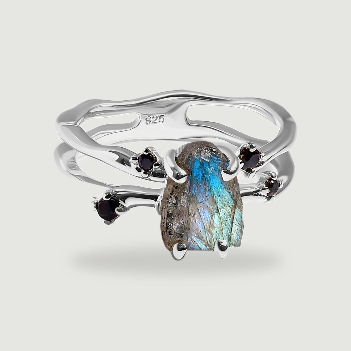 A sterling silver ring holds a raw blue-green labradorite between four black accent stones on a light gray background.