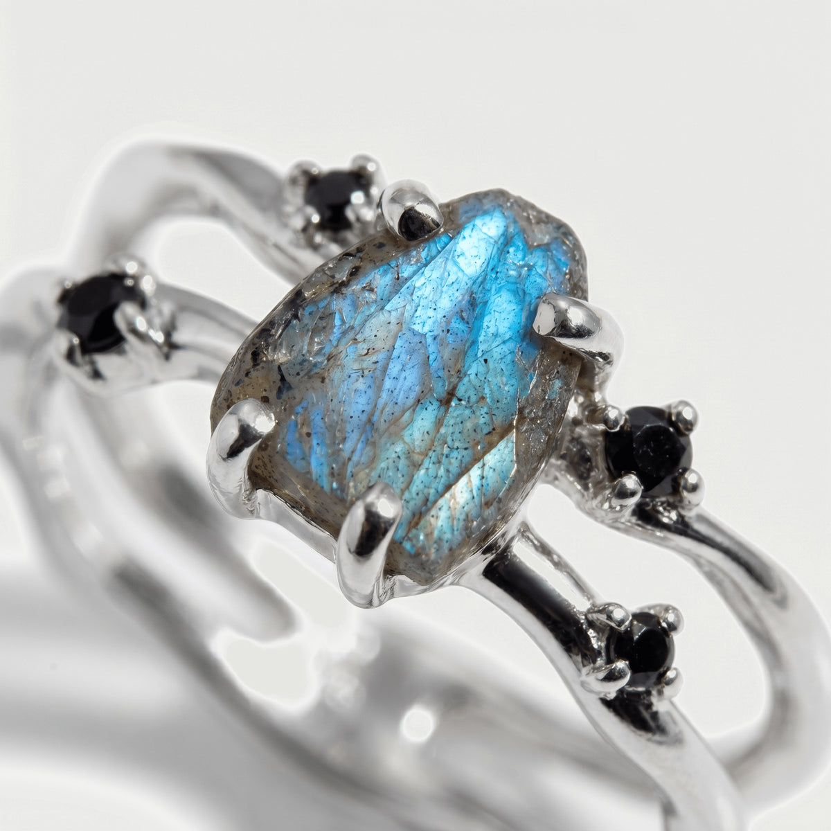 A close view shows the blue sheen, natural surface lines, silver prongs, and black accent stones of the labradorite ring.