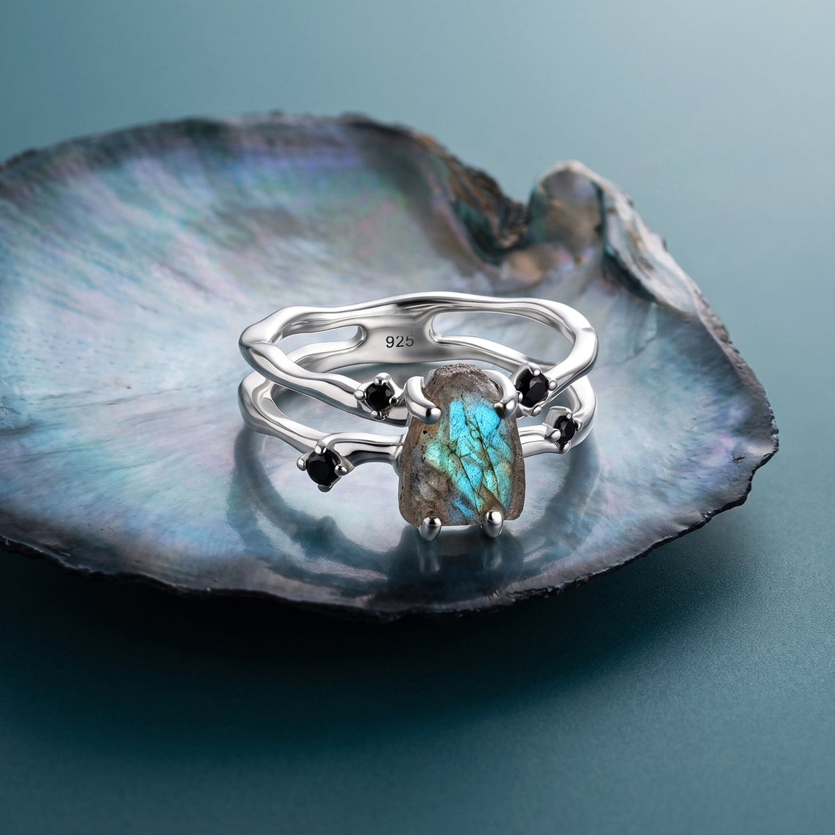 The silver labradorite ring rests on an iridescent shell with its open band and black accents visible.