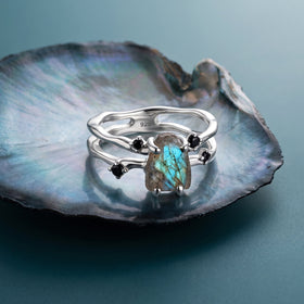 The silver labradorite ring rests on an iridescent shell with its open band and black accents visible.
