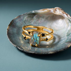 The yellow gold labradorite ring is arranged on a pearly shell over a clean blue tabletop.