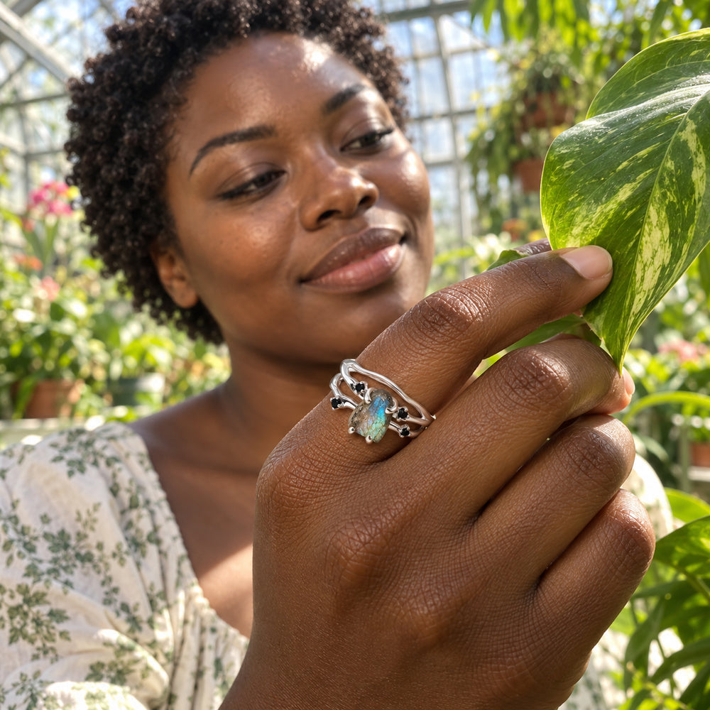 A woman wears the silver labradorite ring while gently holding a green leaf in a sunlit greenhouse.