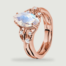 A rose gold vermeil ring stands at an angle with a blue flashing moonstone and small clear stones along its shoulders.