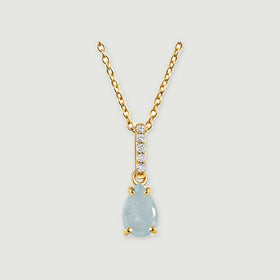 A pale blue pear-shaped aquamarine pendant hangs from a yellow gold chain above a soft gray background.