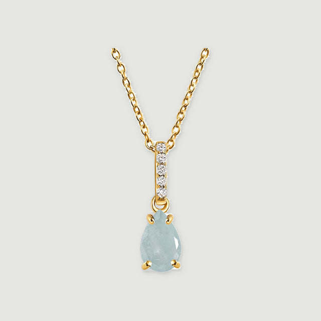 A pale blue pear-shaped aquamarine pendant hangs from a yellow gold chain above a soft gray background.
