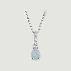 A silver necklace displays a light blue pear-shaped stone held by four prongs on a pale gray surface.