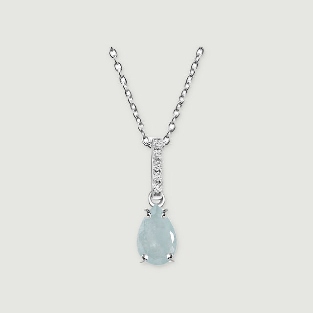 A silver necklace displays a light blue pear-shaped stone held by four prongs on a pale gray surface.