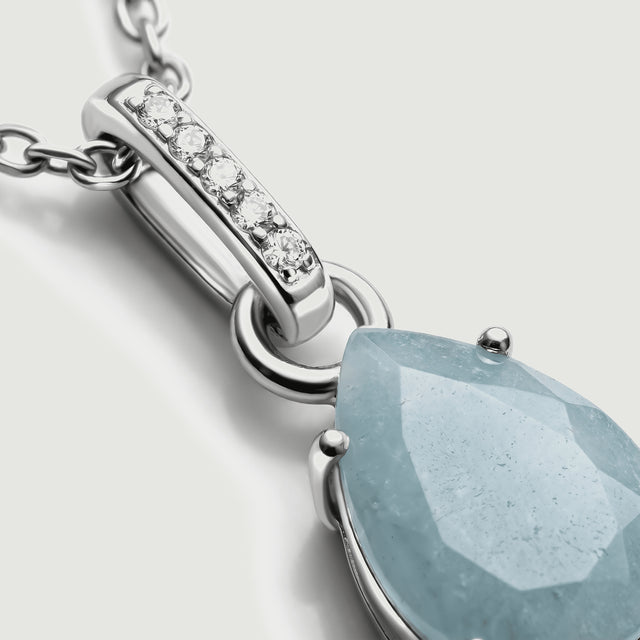 Five round clear stones line the silver bail beside the textured facets of the pale blue pendant.