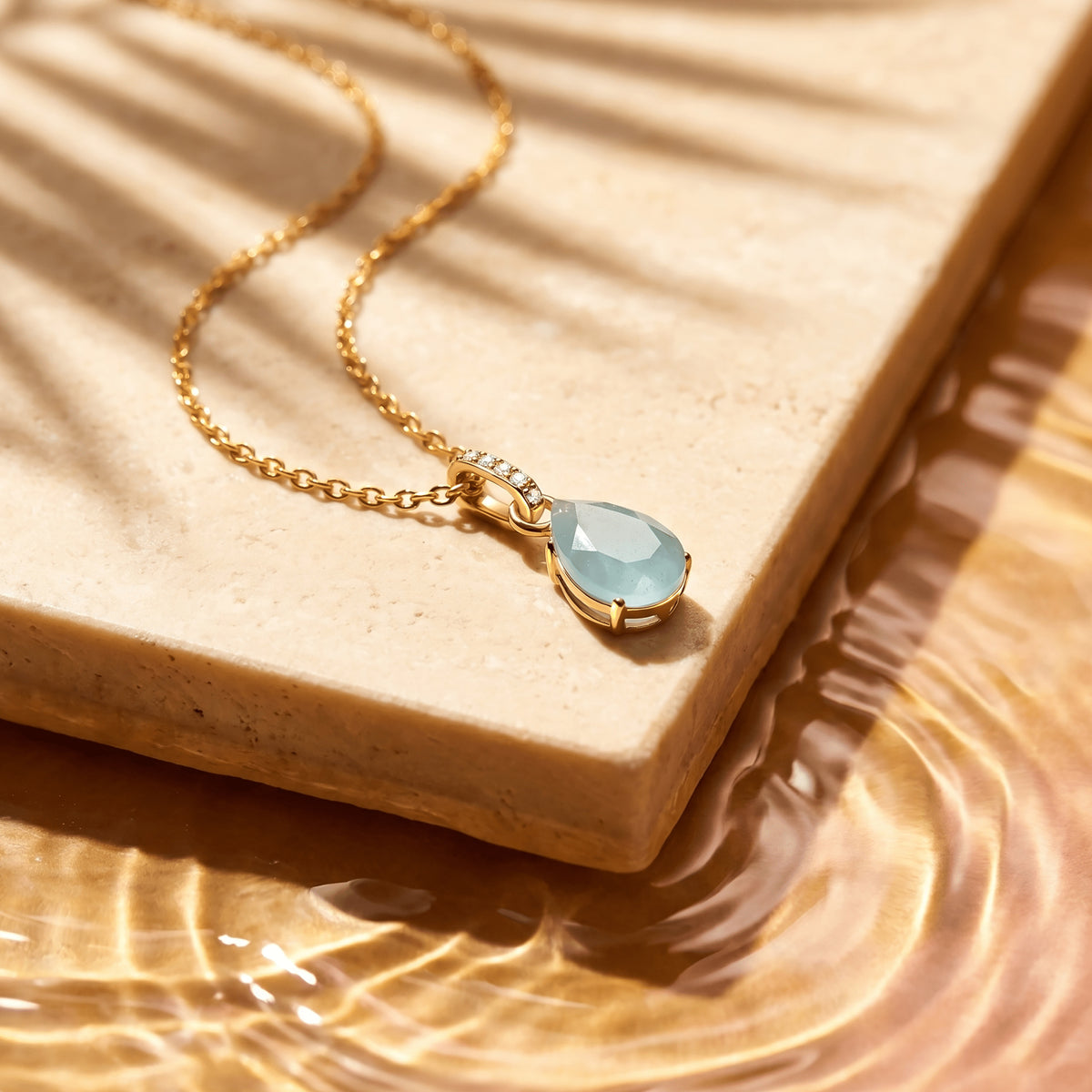 The yellow gold necklace rests diagonally on a cream stone slab with sunlight across the tabletop.