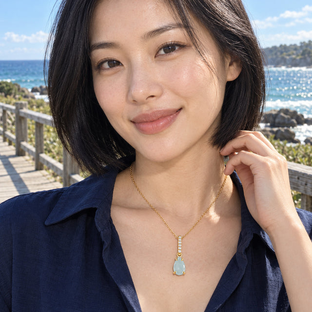 A woman in a navy shirt wears the yellow gold aquamarine necklace beside a seaside boardwalk.