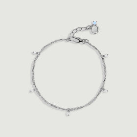 A silver anklet forms an oval with five dangling pearls and a lobster clasp on light gray.
