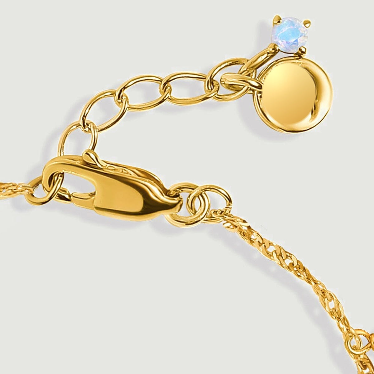 The gold lobster clasp, oval extender links and small pale blue end stone are shown in close detail.