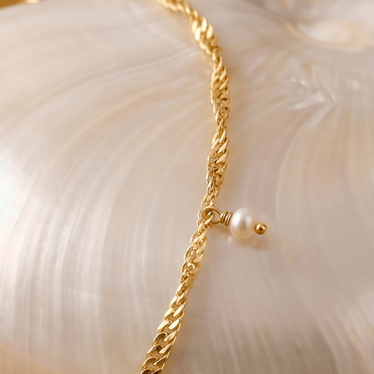 A small pearl drop hangs from the gold chain as it crosses the curved side of a white shell.