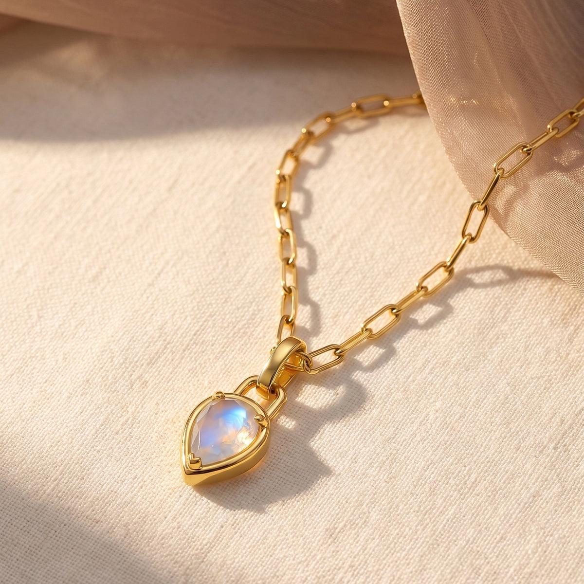 A gold-tone link necklace lies diagonally on woven fabric with a blue-white pear-shaped pendant.