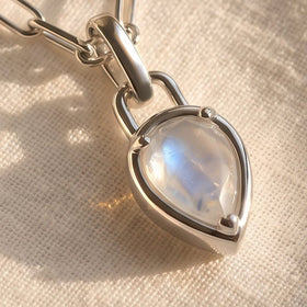 An angled close-up reveals the raised silver-tone rim around the pear-shaped moonstone on textured fabric.