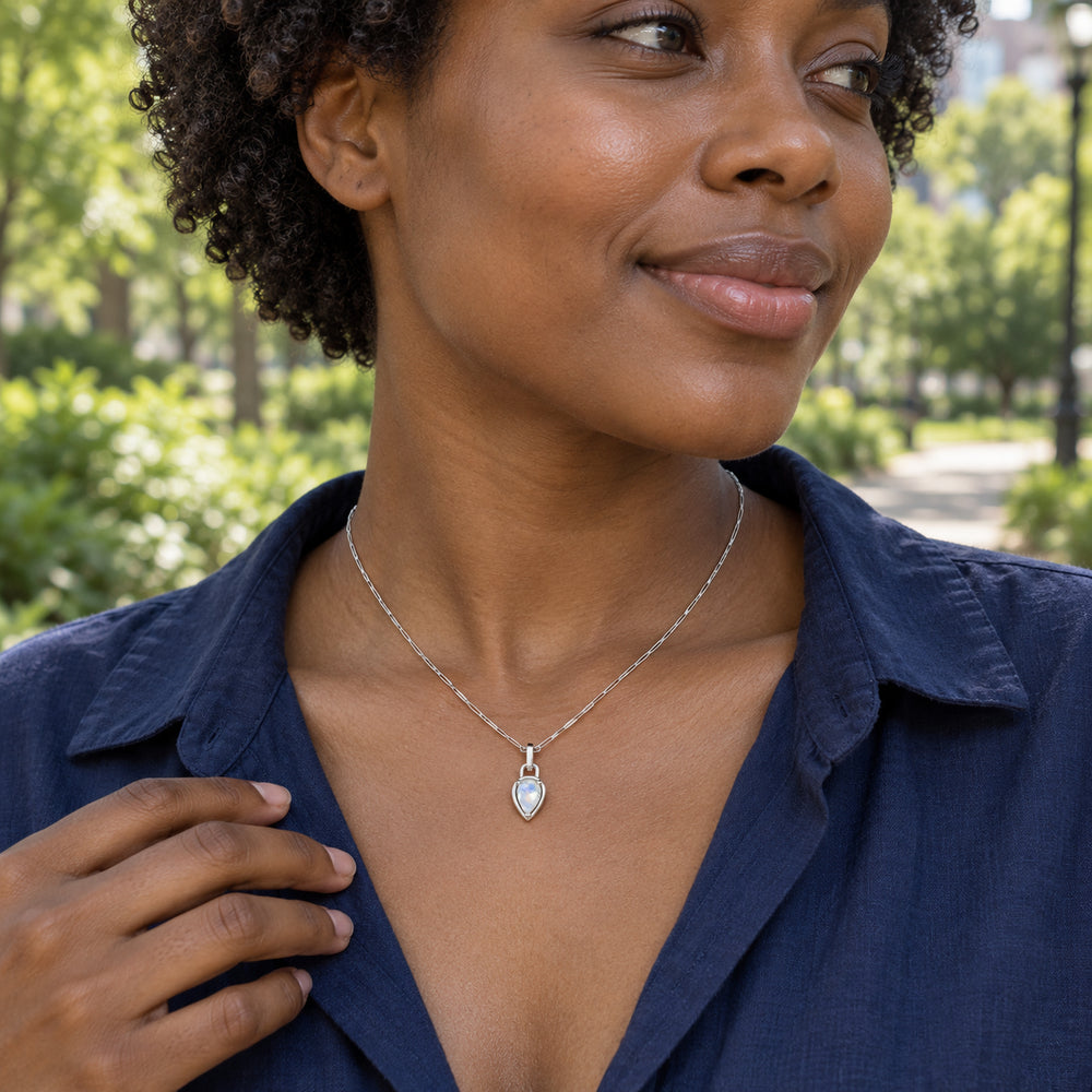 A woman in a navy blouse wears the silver-tone moonstone necklace in a leafy park with her hand resting near the collar.