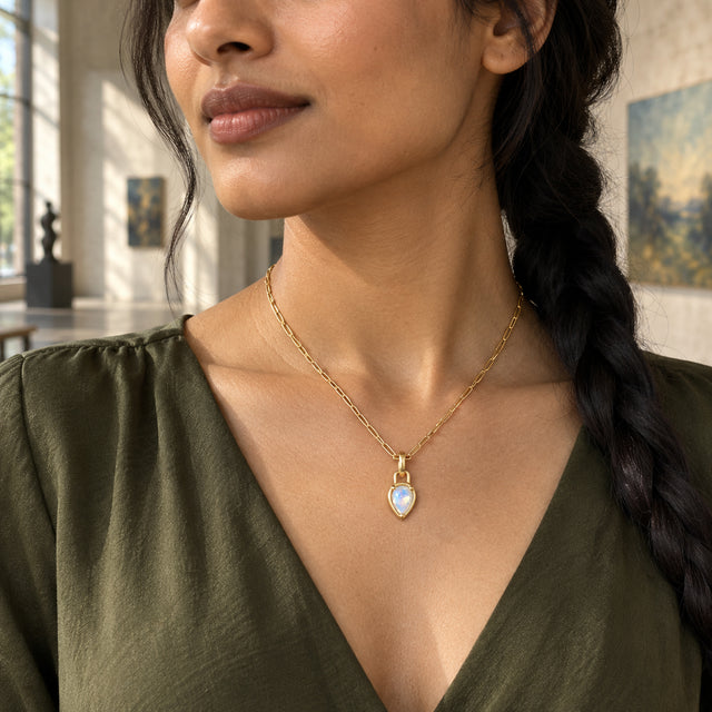 A woman with a dark braid wears the gold-tone pear-shaped moonstone necklace above an olive V-neck blouse in an art gallery.