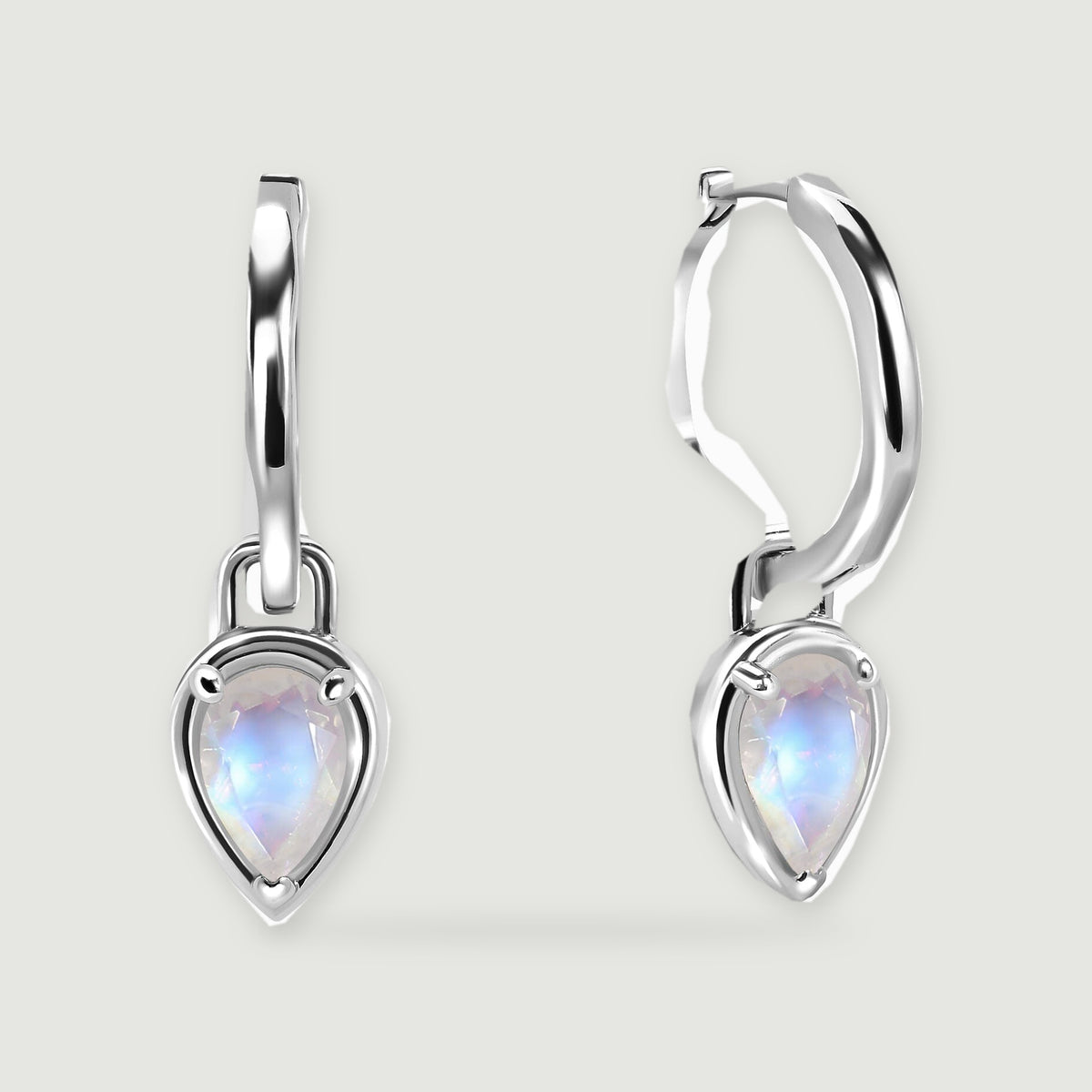 Two polished silver-tone hoop earrings have pear-shaped moonstone drops on a light grey surface.