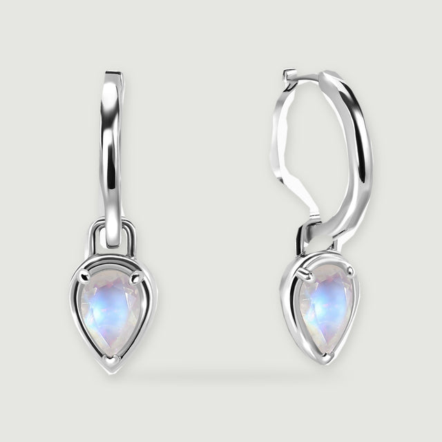 Two polished silver-tone hoop earrings have pear-shaped moonstone drops on a light grey surface.