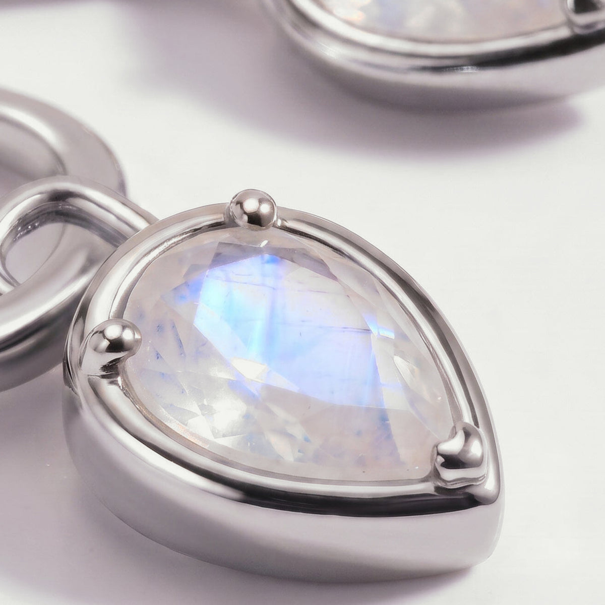 A close view shows blue reflections across a pear-shaped moonstone held by three silver-tone prongs.