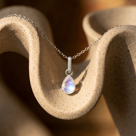 The silver necklace rests over a curved speckled ceramic surface with its moonstone pendant in warm daylight.