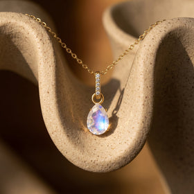 A yellow gold vermeil chain follows a curved ceramic surface while the pear-shaped moonstone catches blue reflections.