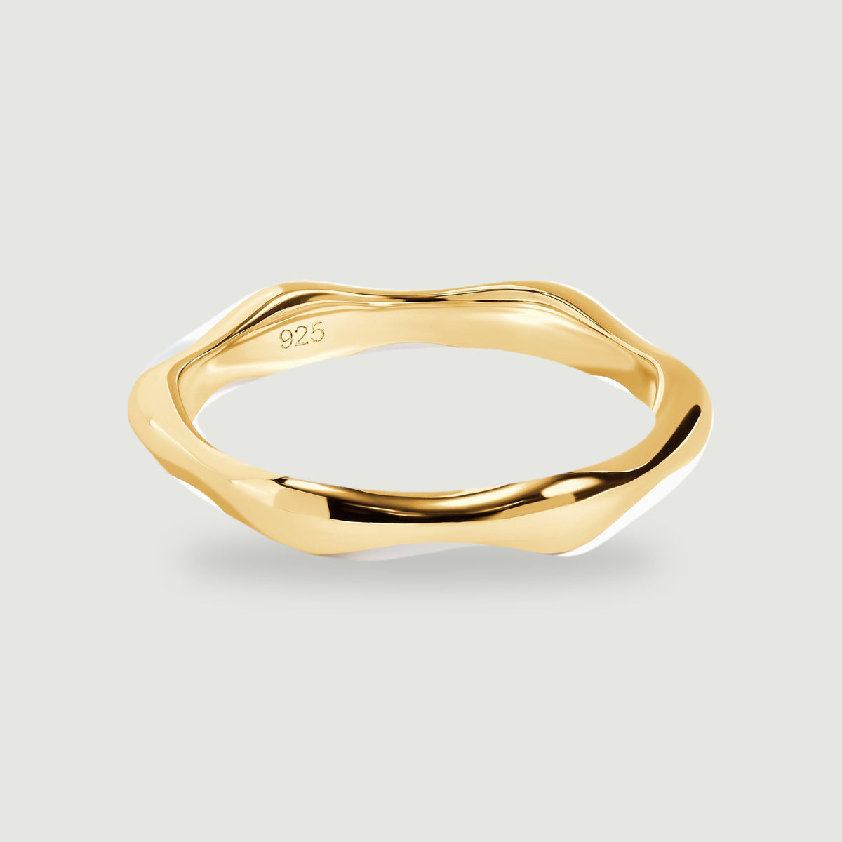 A polished yellow gold ring with an undulating band rests on a light gray surface.