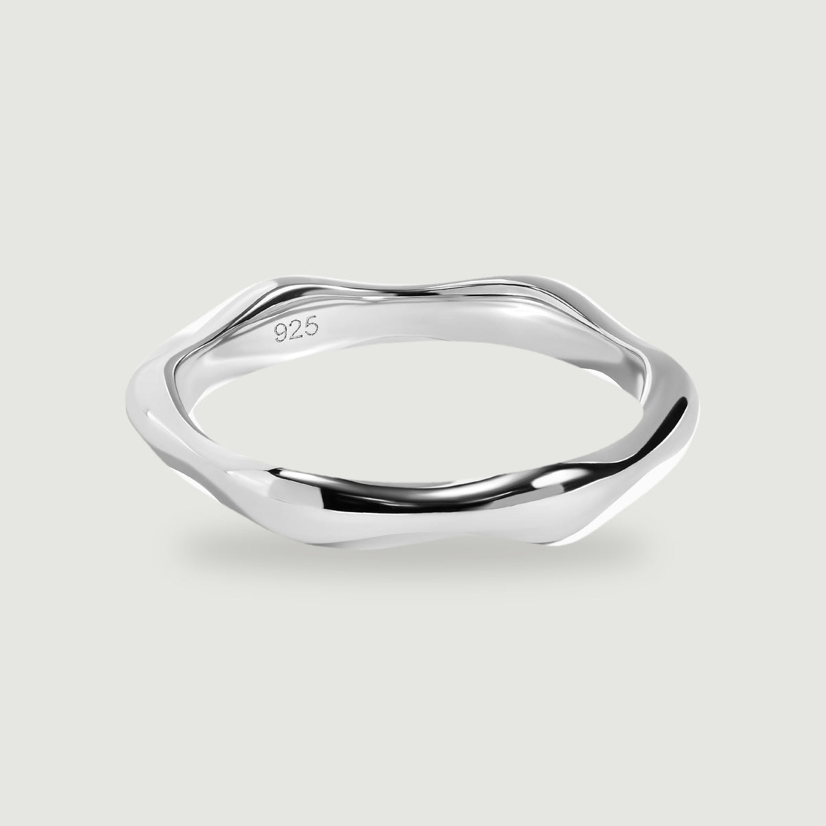 A polished silver ring with an undulating band rests on a light gray surface.