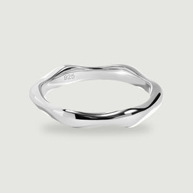 A polished silver ring with an undulating band rests on a light gray surface.