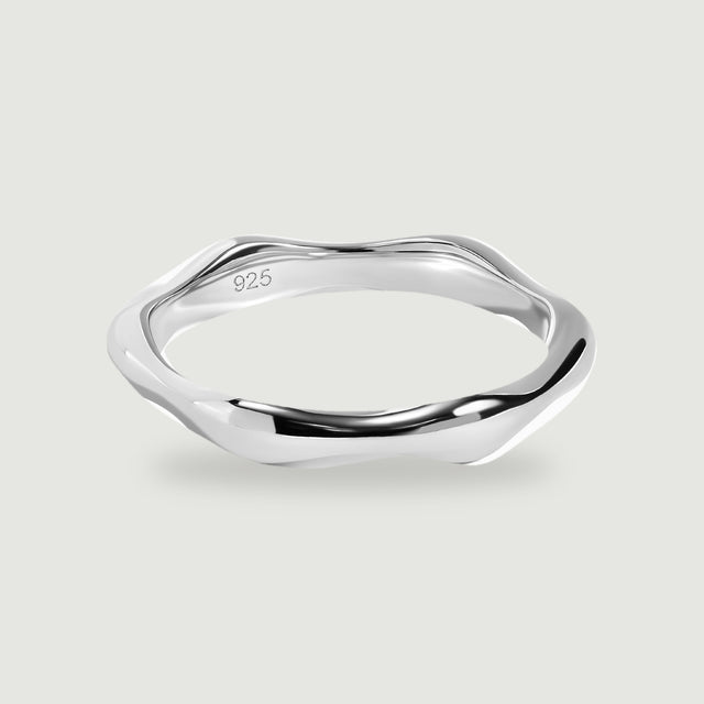 A polished silver ring with an undulating band rests on a light gray surface.