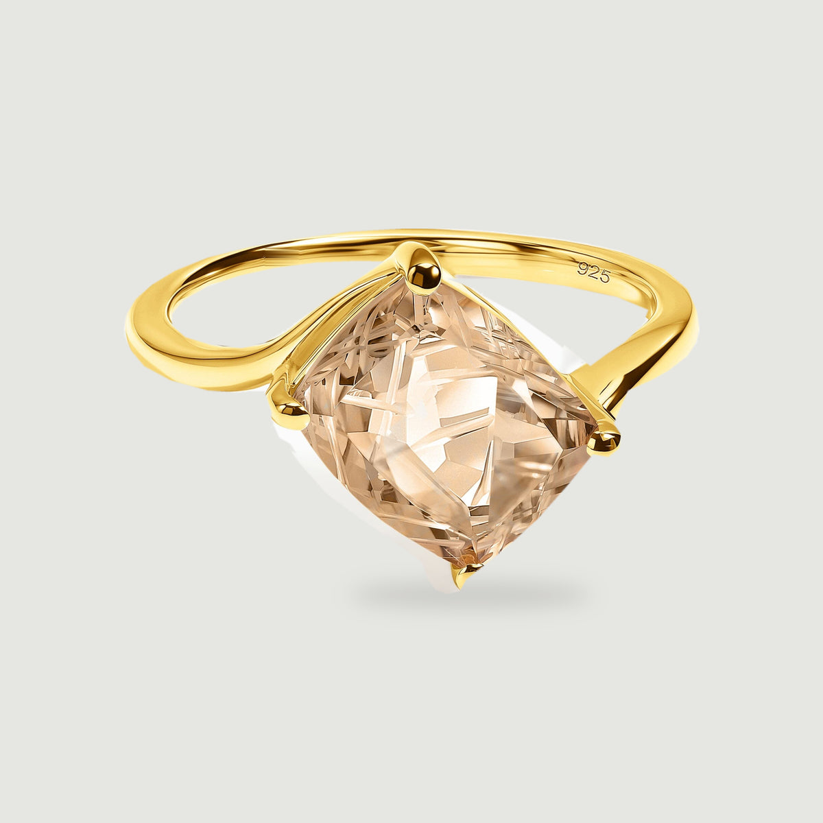 A yellow gold vermeil ring holds a tilted rectangular champagne quartz with carved facets on a light gray surface.