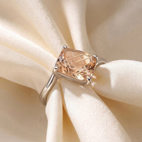 A silver champagne quartz ring lies across pale fabric folds with all four prongs visible.