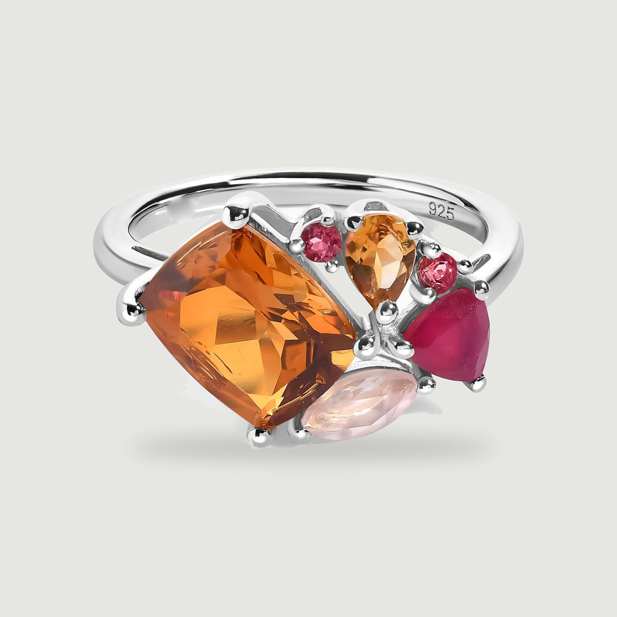 A silver ring with polished prongs holds an orange gemstone and an asymmetric cluster of pink stones.