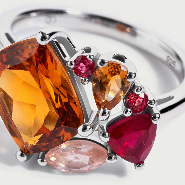 Bright silver prongs frame an amber pear shaped stone and two small round pink stones beside the larger orange gem.