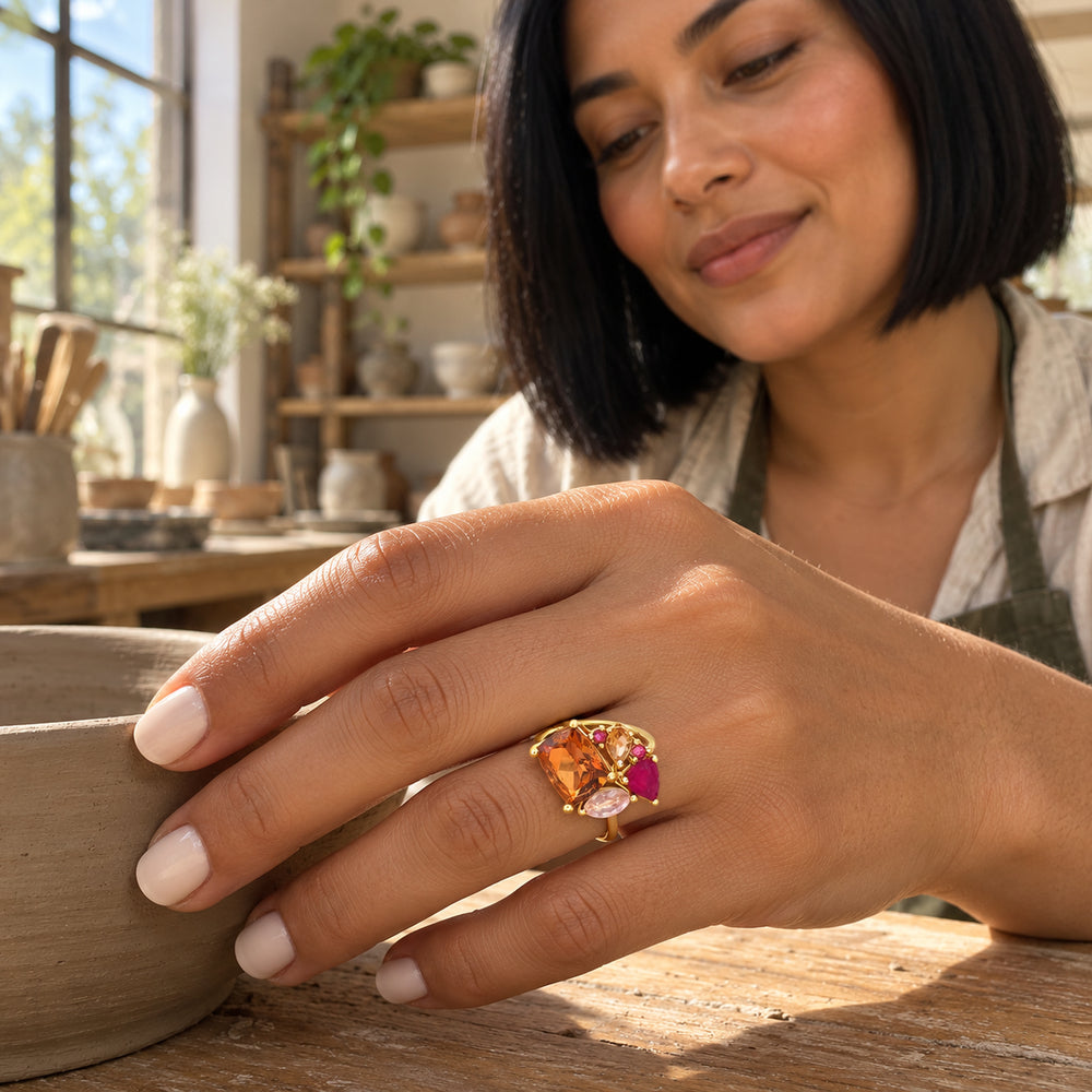 A woman with a dark bob wears the yellow gold gemstone ring while resting her hand on a clay bowl in a sunlit workshop.