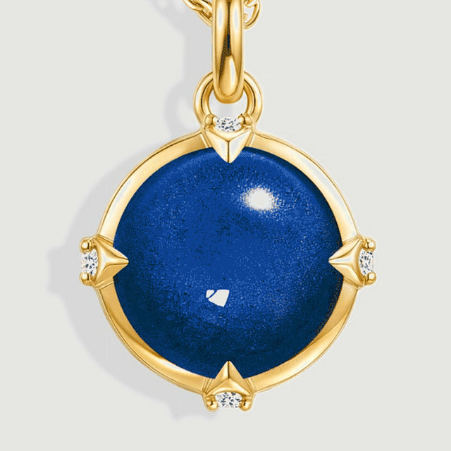 The domed blue cabochon is shown close up with four small clear accents and a polished yellow gold rim.