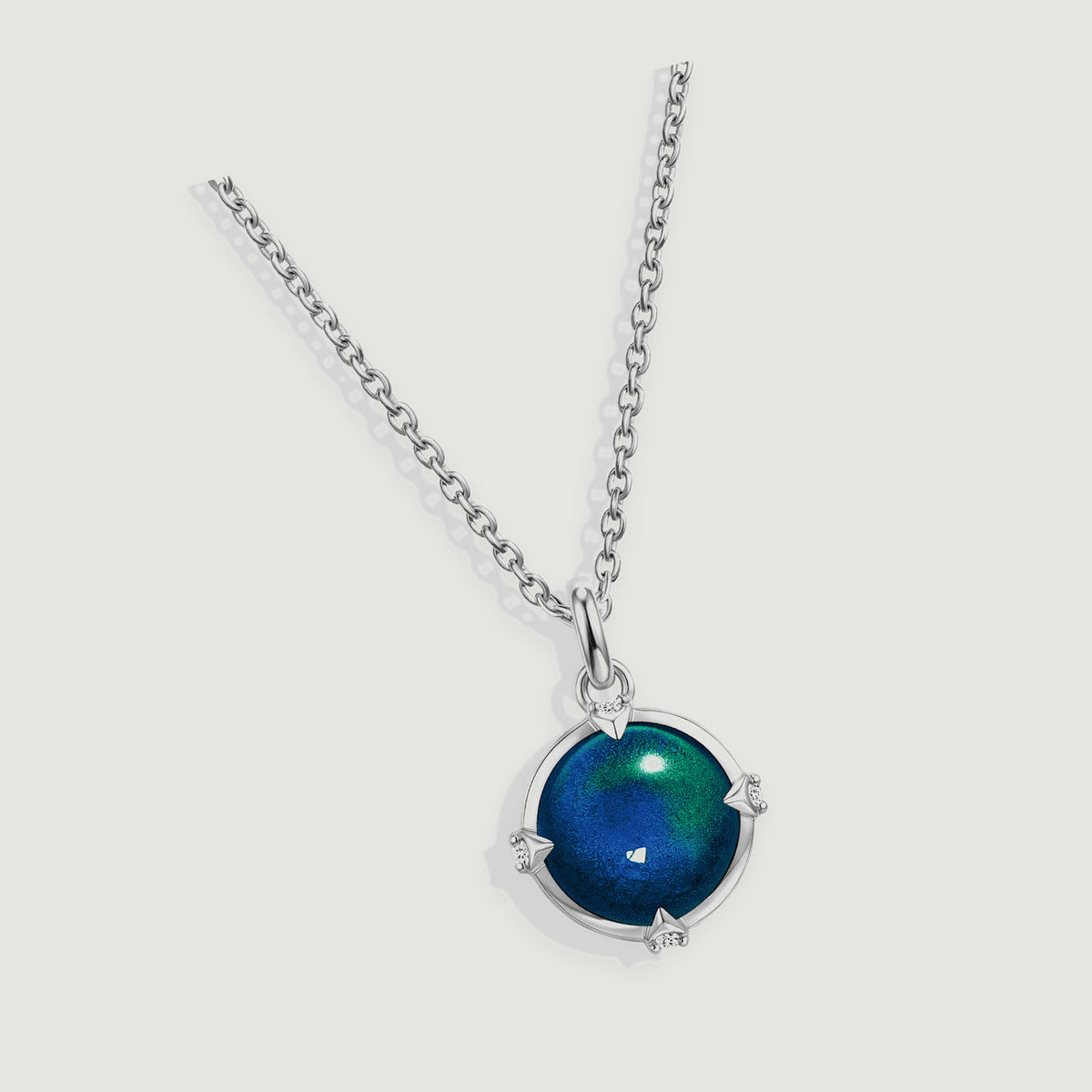 A silver pendant necklace lies diagonally across a light gray surface with a multicolored round stone.