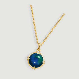 A yellow gold pendant necklace lies diagonally across a light gray surface with a multicolored round stone.