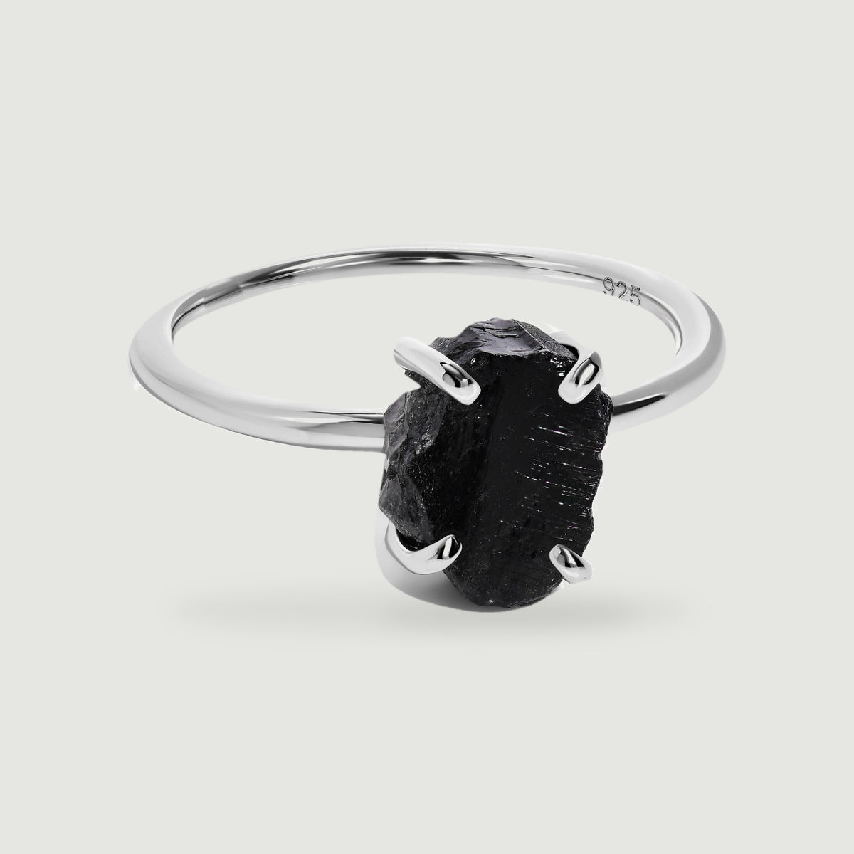 A raw black obsidian stone rests in four silver prongs on a slender polished ring against a light gray background.
