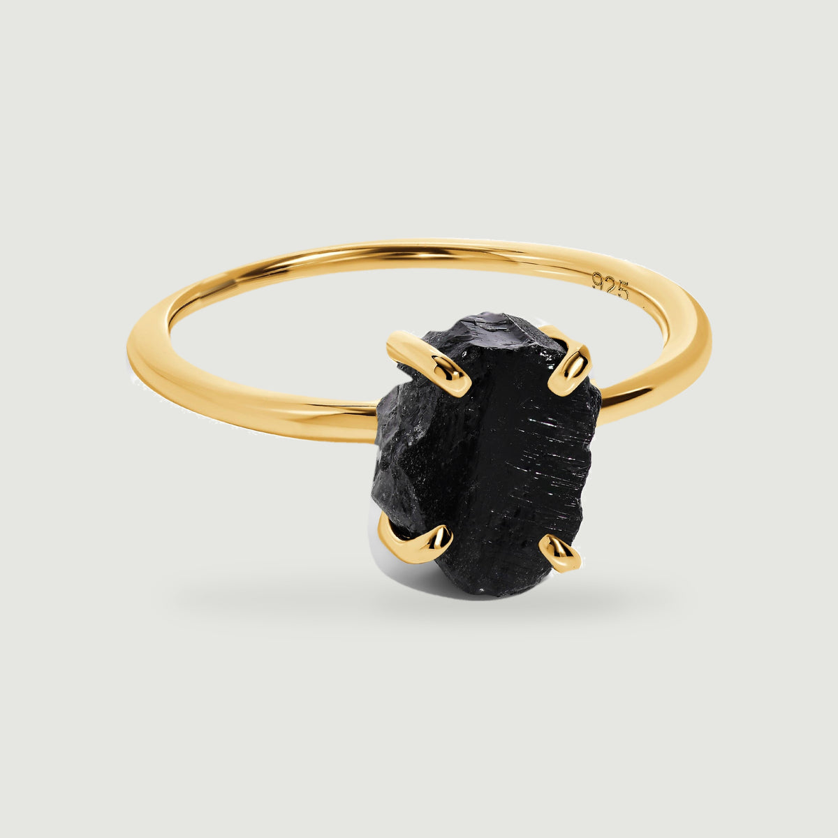A yellow gold vermeil band curves behind a rough black obsidian stone held by four rounded prongs.