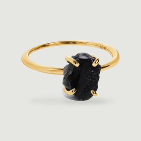 A yellow gold vermeil band curves behind a rough black obsidian stone held by four rounded prongs.