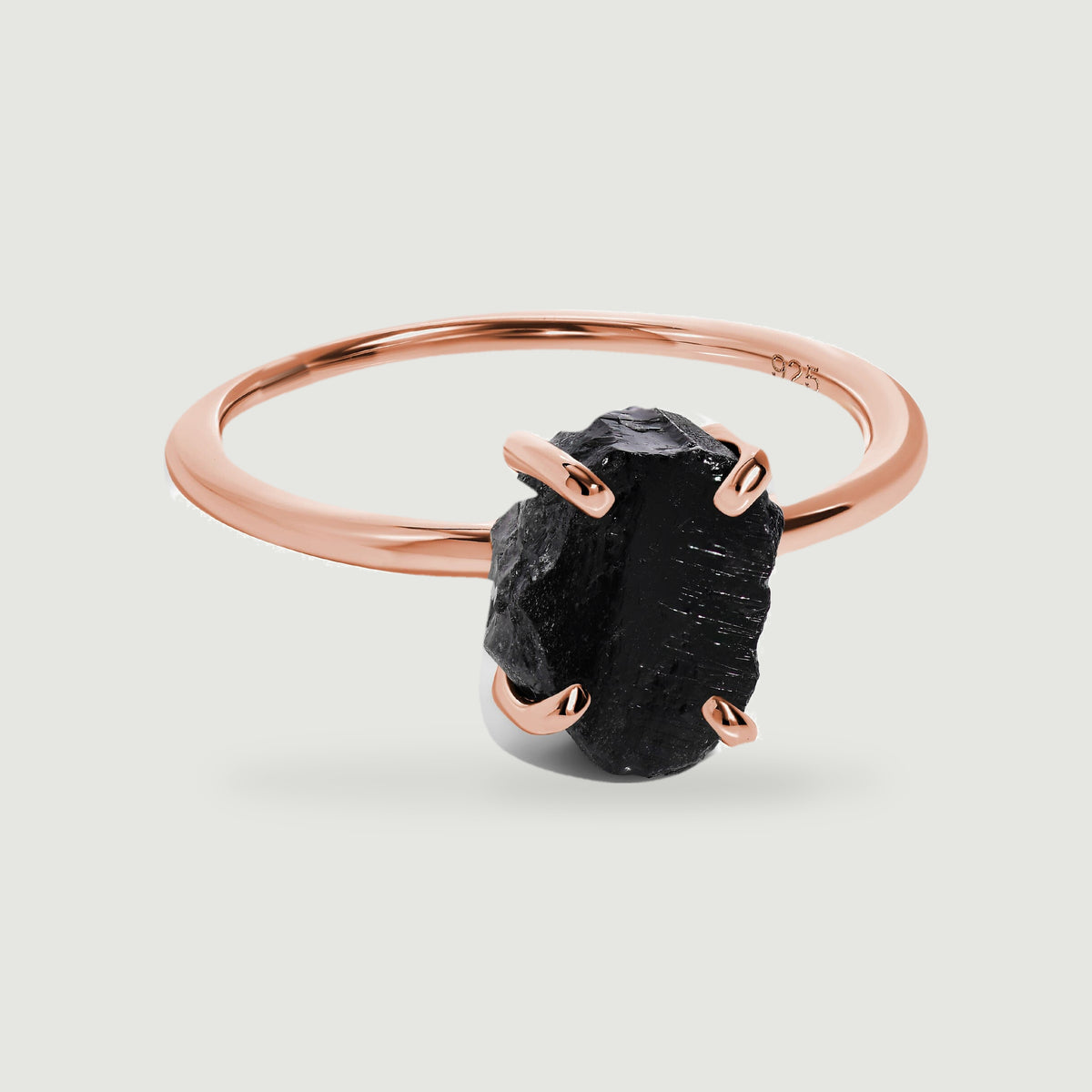 A rose gold vermeil ring with a textured black obsidian stone is centered on a pale gray surface with a soft shadow.