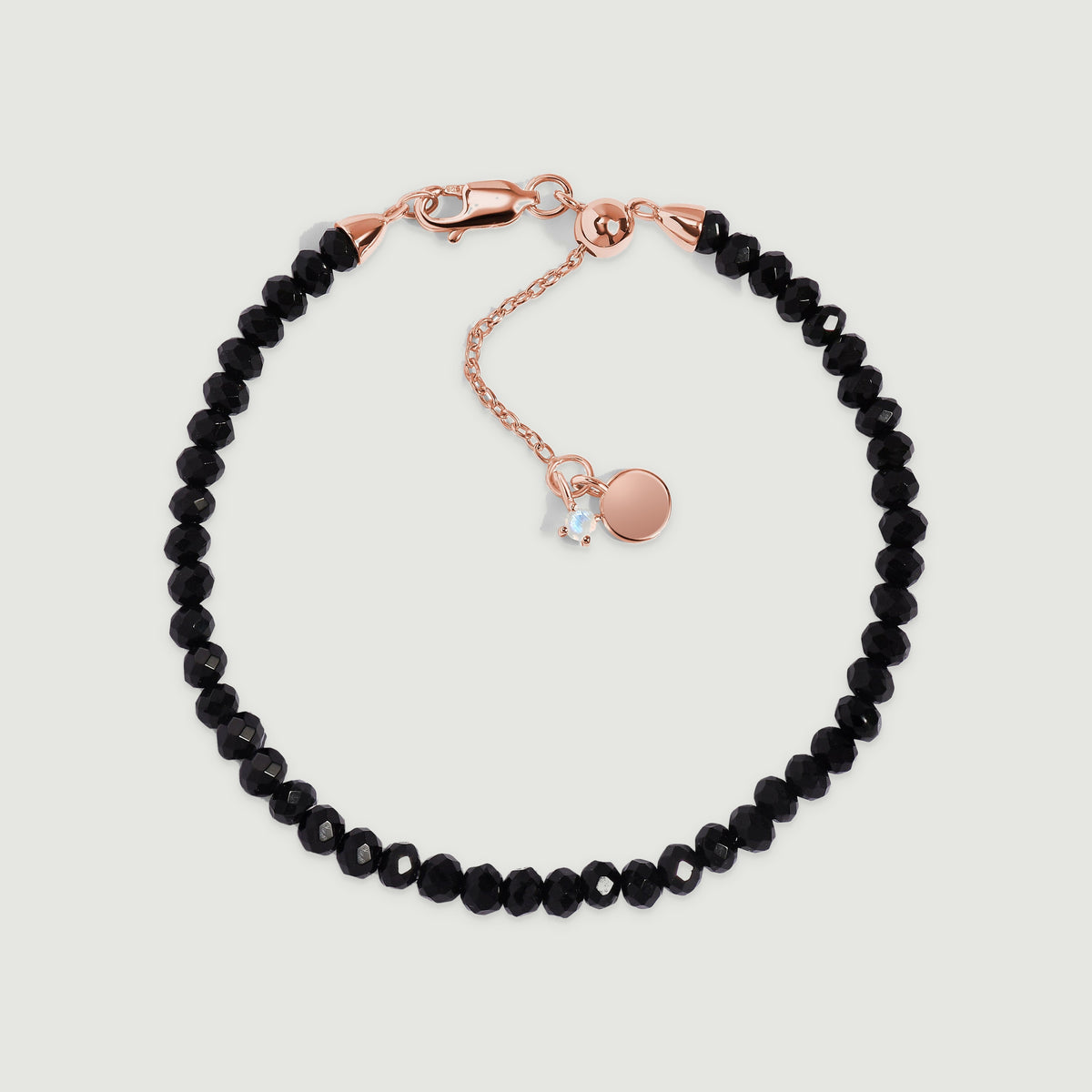 A black obsidian bracelet with rose gold vermeil fittings is centered on a pale gray surface.