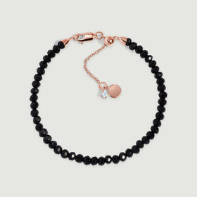 A black obsidian bracelet with rose gold vermeil fittings is centered on a pale gray surface.